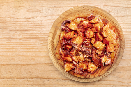 Pulpo a la gallega, octopus with potatoes and paprika, a typical Spanish Galician dish, on a traditional wooden plate, shot from the top on a wooden background with a place for textの写真素材