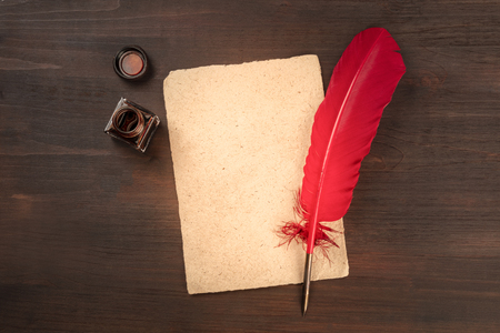 A vintage background with a quill pen on a piece of old parchment paper, with an ink well, shot from above on a dark wooden background with a place for textの写真素材