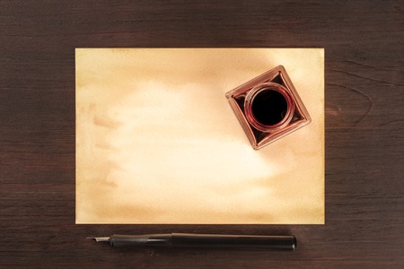 A vintage background with old paper, a nib pen and an ink well, shot from above on a dark wooden background with a place for textの写真素材