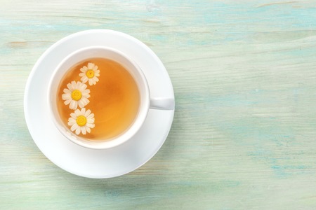 An overhead photo of a cup of chamomile tea on a teal blue background with copyspaceの写真素材