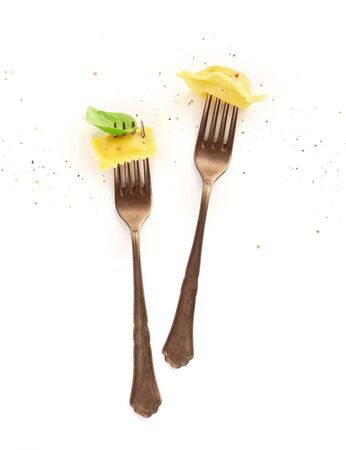 Two forks with different ravioli, basil leaf and pepper on a white backgroundの写真素材