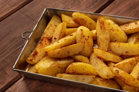 Potato wedges, oven roasted, in a baking tray on a rustic backgroundの写真素材