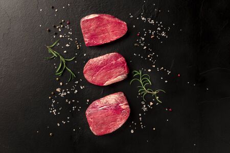 Raw sirloin beef steaks with salt, pepper and rosemary on a black background with a place for textの写真素材