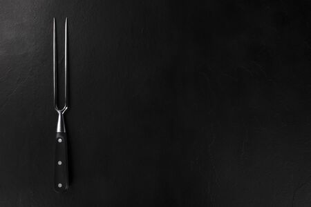 A carving fork, overhead shot on a black background with a place for textの写真素材
