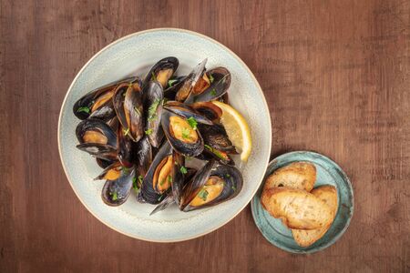Marinara mussels, moules mariniere, overhead shot on a dark rustic wooden background with toasted bread and copyspaceの写真素材