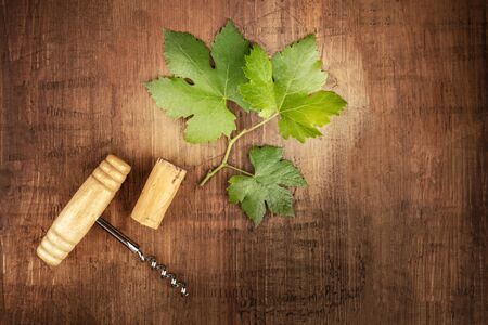 Wine design template. A vine leaf with a vintage corkscrew and a cork, shot from the top on a dark rustic wooden background with a place for textの写真素材