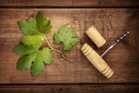 A vine leaf with a vintage corkscrew and a cork, shot from above on a dark rustic wooden backgroundの写真素材