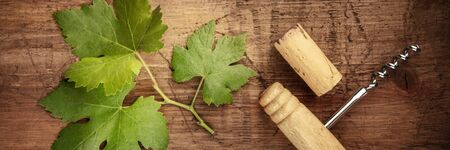 A vine leaf with a vintage corkscrew and a wine cork, overhead panoramic shot on a wooden barrelの写真素材