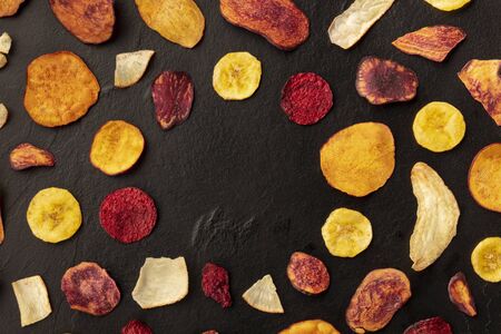 Dry fruit and vegetable chips, healthy vegan snack, an organic food flat lay pattern on a black background, forming a frame with a place for textの写真素材