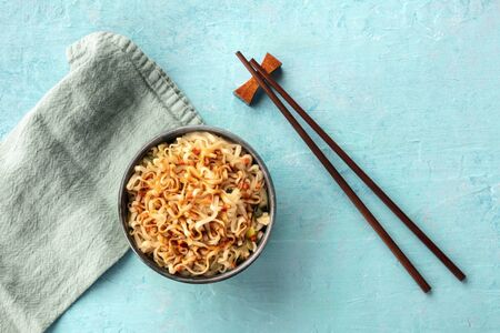 Instant ramen noodles with carrot and a sauce, shot from the top on a teal blue background with chopsticks and a place for textの写真素材