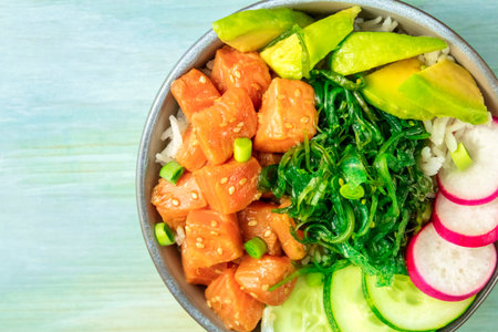 Salmon poke with avocado, wakame and cucumber, overhead close-up shot on a teal blue background with...