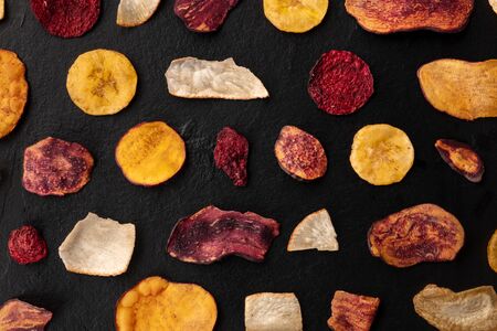 Dry fruit and vegetable chips, overhead shot. Healthy vegan snack, an organic food flat lay pattern on a black backgroundの写真素材
