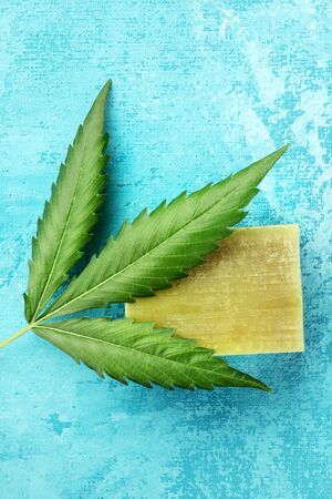 A cannabis leaf with homemade hemp soap bar, shot from above on a turquoise blue background with a place for textの写真素材