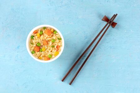 Ramen cup, instant noodles in a plastic cup, overhead shot with chopsticks and a place for text on a blue backgroundの写真素材