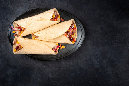 Burrito sandwich wraps, top shot on a black background. Tortillas stuffed with ground beef meat,...