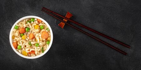 Ramen cup panorama, instant noodles in a plastic cup, overhead flat lay shot with chopsticks and copy space on a dark backgroundの写真素材