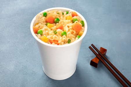 Ramen cup close-up, instant soba noodles in a plastic cup with green peas and carrot slices, with...