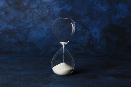 Time is running out concept. An hourglass with sand falling through, on a dark blue background with a place for textの写真素材