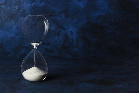 Time is running out concept. An hourglass with sand falling through, on a dark blue background with copy spaceの写真素材