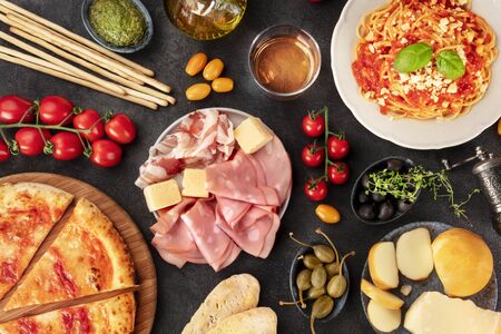 Italian food. Pizza, pasta, cheese, ham, wine, olives, pesto, olive oil, capers, shot from above with a place for text, a flat lay on a dark backgroundの写真素材