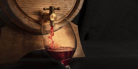 A panorama of pouring wine into a glass from a barrel, a close-up on a dark background with copy spaceの写真素材