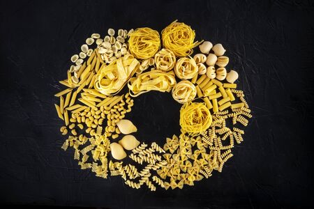 Italian pasta wreath with copy space, a flat lay of a variety of pasta types, shot from the top on a black background with a place for textの写真素材