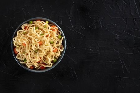 Instant noodles bowl with carrot and scallions, shot from above on a black background with a place for textの写真素材