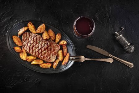 Grilled beef steak with baked potato wedges and red wine, shot from the top on a black backgroundの写真素材