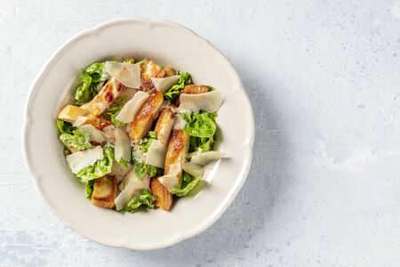 Caesar salad. Grilled chicken breast slices, green romaine salad leaves, croutons and parmesan, the classic recipe on a white marble background with a place for textの写真素材
