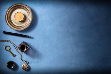 Vintage background with copy space, with an old watch, a key, ink well and pen, and a candle, a flat...