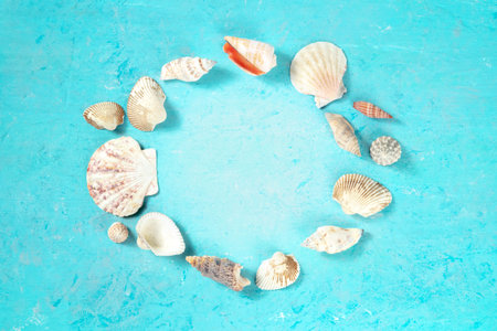 Sea shells in a wreath, forming a frame on a tuquoise blue background with a place for text