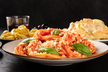 Pasta with tomato sauce, basil and Parmesan, a close-up in a restaurant with other blurred food and wine in the dark background