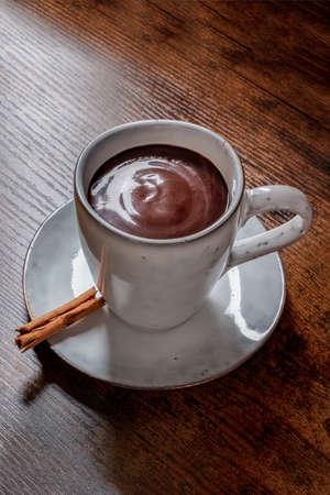 Hot chocolate in a cup, with a cinnamon stick, on a rustic wooden backgroundの写真素材