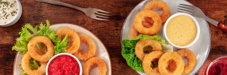 Calamari rings panorama. Squid rings with wine and various sauces, top flat lay shot on a dark rustic wooden tableの写真素材