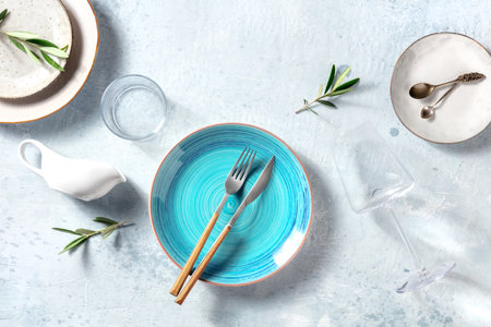 Trendy tableware with a blue plate, shot from the top. Dinnerware set for dinner, with olive branches for decor, Mediterranean food concept. Elegant dishes, overhead flat lay shotの写真素材