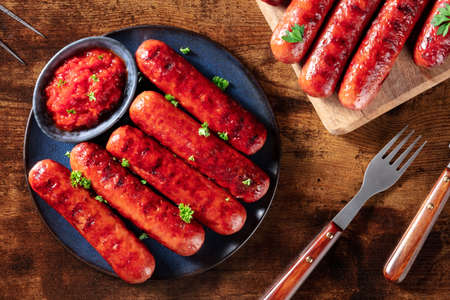 Cooked sausages with ketchup, shot from the top on a dark rustic wooden table. Delicious barbecue food mealの写真素材