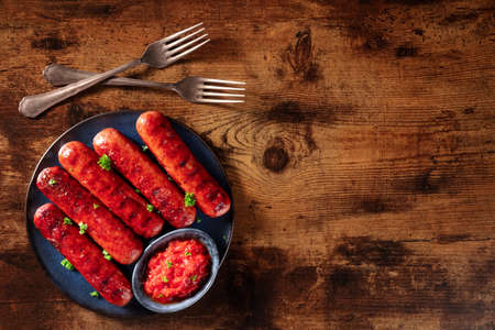 Sausages with ketchup and two forks, shot from the top on a dark rustic wooden background with copy space. Barbecue foodの写真素材
