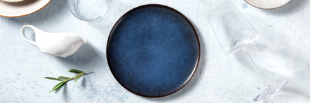 Dinnerware panorama with a blue plate, olive branch, a trendy wine glass and a sauce boat, overhead...
