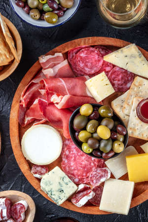 Italian antipasti or Spanish tapas with wine. Gourmet charcuterie and cheese board, shot from above on a black background. Salmon sandwiches, salami, Parma ham, blue cheese. Mediterranean buffetの写真素材