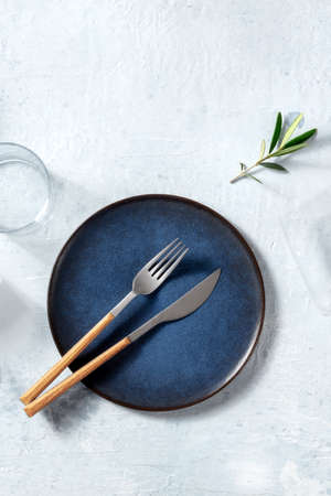 Blue ceramic plate, shot from the above with cutlery and an olive branch, Mediterranean cuisine concept with copy space, a flat layの写真素材