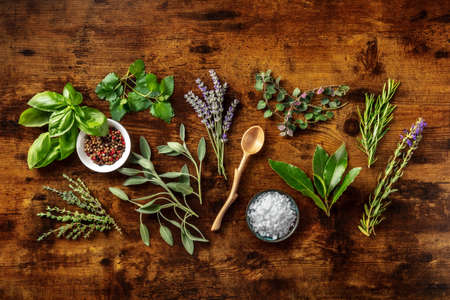 Fresh aromatic herbs, overhead flat lay shot on a rustic wooden background with spices. Bunches of rosemary, basil, thyme, lavender, and various other culinary plantsの写真素材