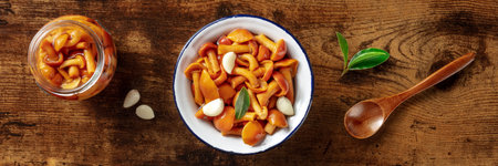 Pickled mushrooms panorama with pepper, garlic, and a bay leaf, overhead flat lay shot on a rustic...