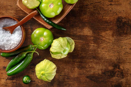 Tomatillos, green tomatoes, and chili peppers. Mexican cuisine ingredients on a dark rustic wooden background, overhead flat lay shot with copy spaceの写真素材