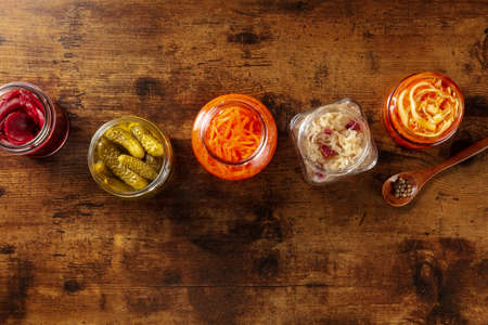 Fermented foods. A variety of pickled vegetables, shot from above with copy space. Homemade preserves in glass jars. Healthy vegan ingredients on a wooden tableの写真素材