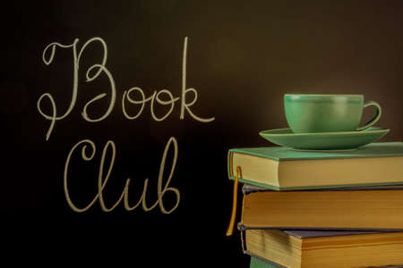 Book Club, toned image. A stack of hardcover books with a cup of coffee and chalk lettering on a blackboardの写真素材