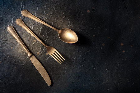 Cutlery. A spoon, a fork, and a knife on a black slate background. Modern silverware on a dark table...