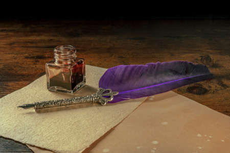 Feather quill pen with a vintage ink well and old paper on a dark rustic wooden backgroundの写真素材