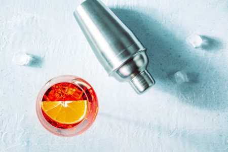 Aperol cocktail with a fresh orange slice, a shaker, and ice cubes, Italian summer cold drink,...