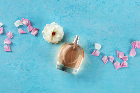Rose fragrance bottle, a luxury product, shot from the top on a blue background with fresh flowers...