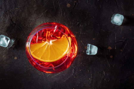 Aperol cocktail with an orange slice and ice cubes close-up, Italian summer cold drink, shot from above on a black slate backgroundの写真素材
